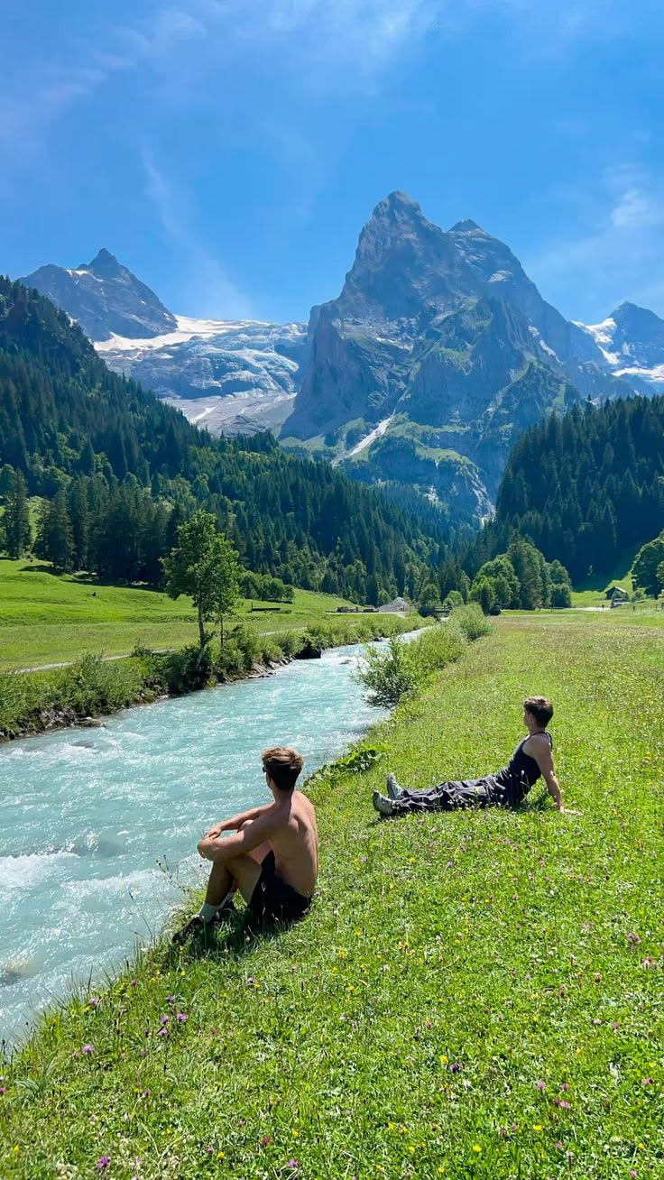Mountain landscape and river with two people resting on the grassy bank